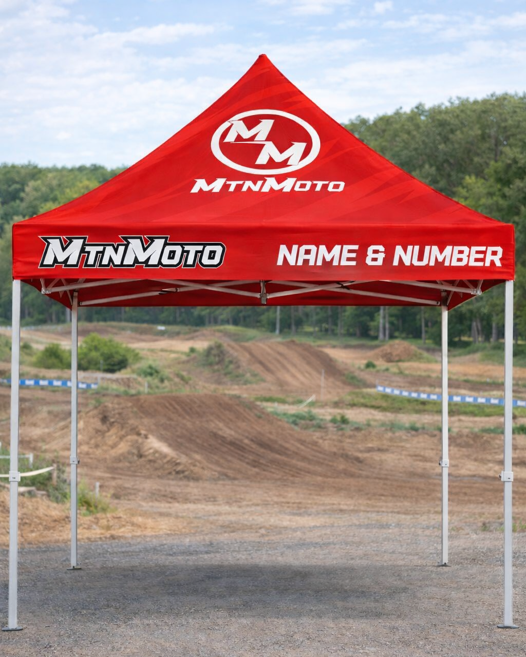 Red MtnMoto tent set up on a dirt track with trees in the background