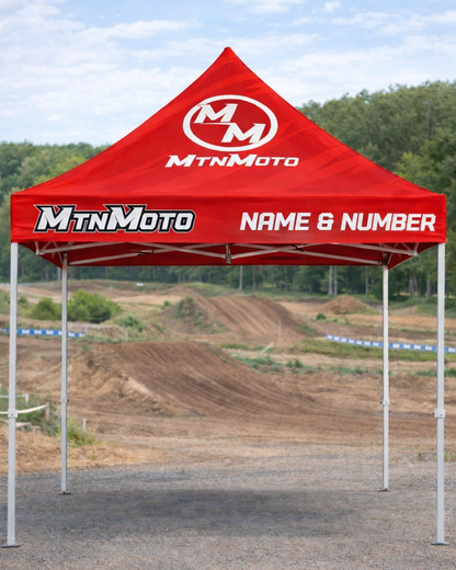Red MtnMoto tent set up on a dirt track with trees in the background